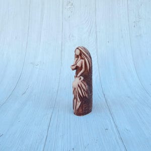 May include: A ceramic figurine of a woman with long hair, holding a small cup in her hand. The figurine is painted in shades of brown and white.