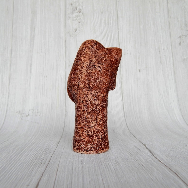May include: A brown ceramic sculpture of a person's head with a textured surface.