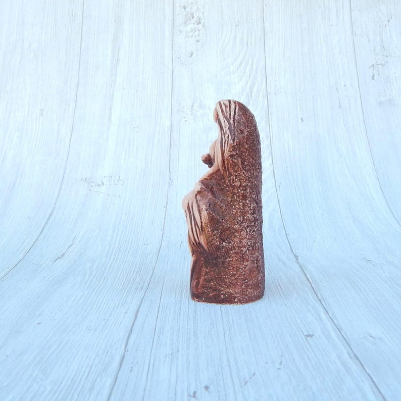 May include: A terracotta sculpture of a woman holding a child. The sculpture is brown and has a rough texture.