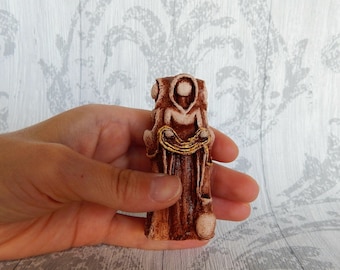 Op de afbeelding: Een klein, bruin keramiek beeldje van een gefiguur in een gewaad dat een gouden touw vasthoudt. Het beeldje staat op een houten oppervlak.
