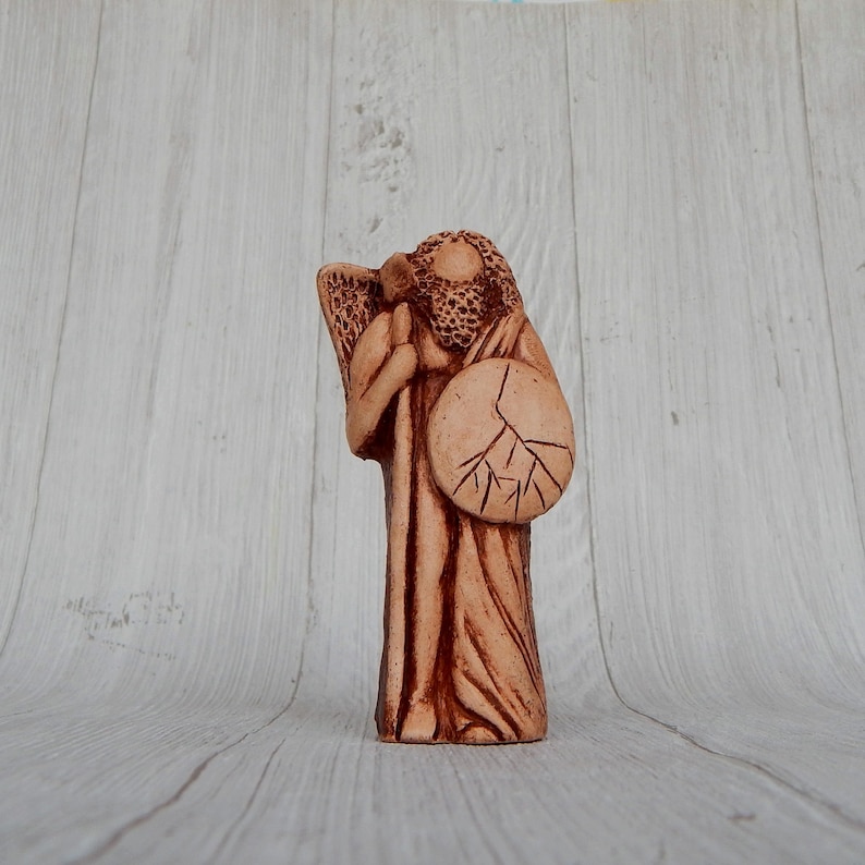 May include: A terracotta figurine of a guardian angel with wings, holding a staff and a shield with a tree design.