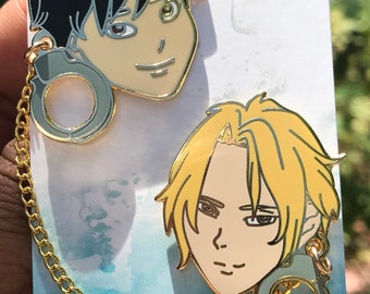 May include: Two gold-colored enamel pins featuring anime characters with a gold chain connecting them. The characters have black and blonde hair and are wearing handcuffs. The pins are on a white background with a blue watercolor effect. The text "Chincha Chingu Etsy" is visible at the bottom of the image.