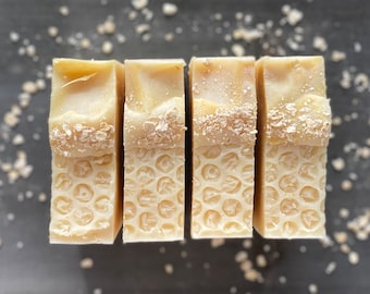 May include: Four bars of handmade soap with a honeycomb pattern and oatmeal on top. The soap is a light beige color.