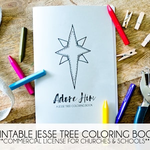 May include: A printable Jesse Tree coloring book with a black and white illustration of a star on the cover. The title "Adore Him" is written in black cursive lettering. The book is surrounded by craft supplies, including crayons, a hole punch, and clothespins.