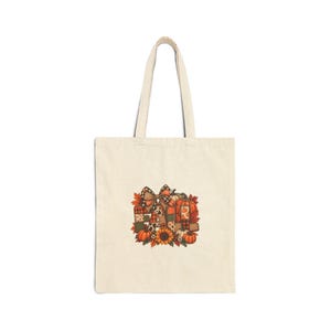 Peut inclure: Un sac fourre-tout en toile beige avec une impression graphique centrale formant le mot FALL. Le motif intègre des citrouilles orange, un tournesol, des feuilles d'automne et un nœud à carreaux, avec des lettres remplies de divers motifs.