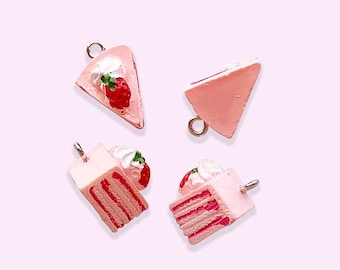 May include: Four miniature cake charms with a pink and white color scheme. Two are triangular slices with a strawberry on top, and two are layered cake slices with whipped cream and a strawberry. Each charm has a silver-colored loop.