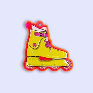 May include: A yellow roller skate charm with pink accents and orange wheels. The charm is made of plastic and has a glossy finish.
