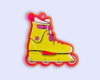 May include: A yellow inline skate charm featuring a bright pink strap, pink laces, and four pink wheels. The skate has a neon orange border and a small circular hole at the top for hanging. The design is flat with a vibrant color palette.