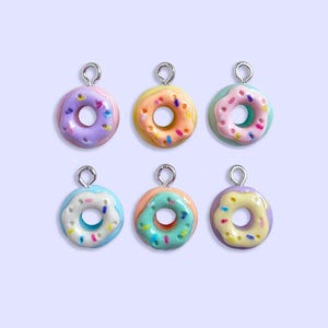 May include: Six colorful donut charms with silver jump rings. The donuts are glazed in pink, yellow, blue, and white with colorful sprinkles.