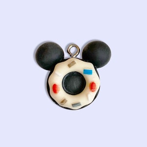 May include: A white and black donut charm with colorful sprinkles, shaped like Mickey Mouse with black ears.