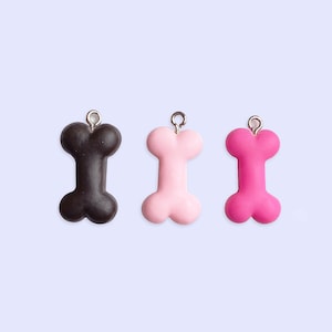 May include: Three dog bone charms, one black, one light pink, and one hot pink.