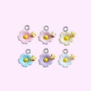 May include: A set of six small flower charms, each featuring a pastel-colored petal design with a yellow center and a tiny attached bee figure. Each charm includes a silver-toned metal jump ring at the top for attachment to jewelry or crafts.