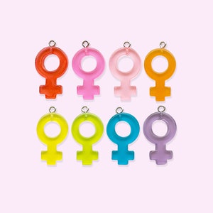 Puede incluir: Ocho abalorios de plástico de colores con forma de símbolo femenino. Los abalorios son de color rojo, rosa, rosa claro, naranja, amarillo, verde, azul y morado.