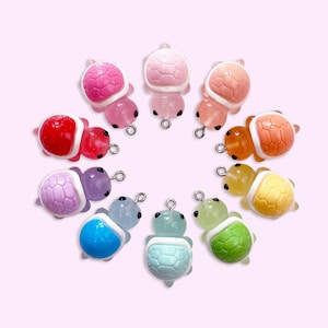 Op de afbeelding: Een set van tien kleurrijke schildpadbedels met witte accenten. De schildpadden zijn in een cirkel gerangschikt, met elke schildpad naar het midden gericht. De schildpadden zijn gemaakt van polymer clay en hebben een glanzende afwerking.