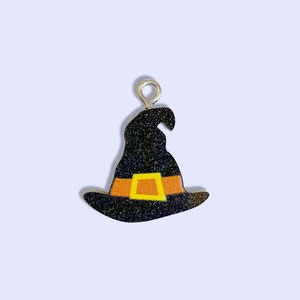 May include: A black witch hat charm with an orange and yellow buckle. The charm has a silver loop for hanging.