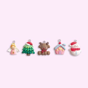 May include: Five Christmas decorations made of clay. The decorations are a green Christmas tree, a brown reindeer, a pink gingerbread house, a white snowman, and a pink angel.