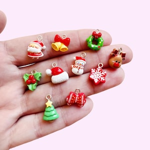 May include: A collection of miniature Christmas-themed charms. The charms include Santa Claus, bells, a wreath, a reindeer, a snowflake, a Christmas tree, and a gift. Each charm is brightly colored and has a small loop for attaching to jewelry or other crafts.