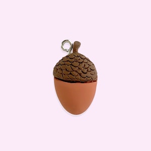 May include: A brown acorn charm with a silver loop. The acorn is made of polymer clay and has a detailed texture.