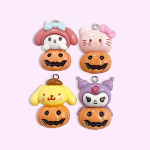 May include: Four Halloween-themed charms featuring popular cartoon characters. Each charm is a character sitting on top of a jack-o'-lantern. The characters are Hello Kitty, My Melody, Cinnamoroll, and Kuromi.