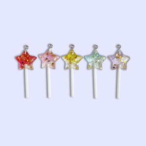 May include: Five star-shaped lollipops with glitter embedded in the candy. The lollipops are in different colors: red, pink, yellow, blue, and purple. Each lollipop is on a white stick.