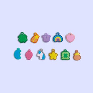 May include: Assortment of 12 colorful charm pendants featuring various shapes and designs, including a heart, a star, a rainbow, a clover, a crescent moon, a cloud, a unicorn, a shooting star, and a pot of gold.