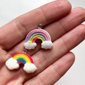 Pu&ograve; includere: Due ciondoli arcobaleno con nuvole bianche, uno con strisce rosa e viola e l'altro con strisce rosse e arancioni. Entrambi i ciondoli hanno un anello d'argento per appenderli.