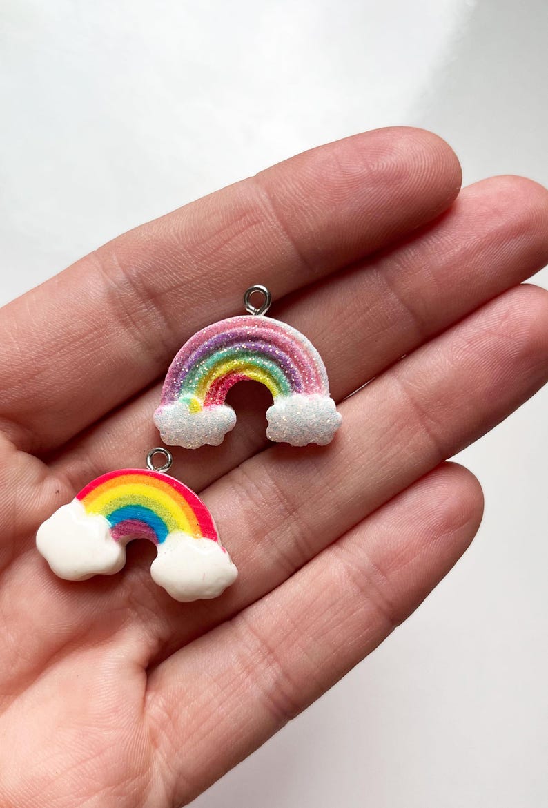 Pu&ograve; includere: Due ciondoli arcobaleno con nuvole bianche, uno con strisce rosa e viola e l'altro con strisce rosse e arancioni. Entrambi i ciondoli hanno un anello d'argento per appenderli.