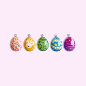 May include: Five colorful Easter eggs with different designs. The eggs are pink with flowers, yellow with a bunny, green with geometric patterns, blue with flowers and hearts, and purple with stars.