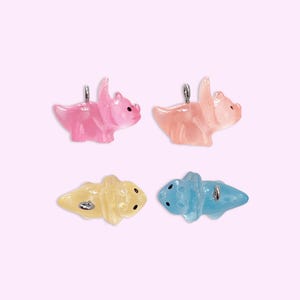 May include: Four translucent dinosaur charms in pink, peach, yellow, and blue. Each charm has a small silver loop for hanging. The charms are shaped like a Triceratops and a long-necked dinosaur.