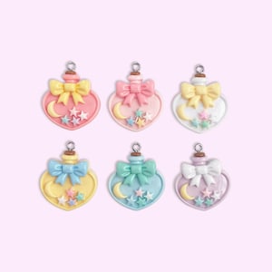 May include: Six pastel heart-shaped charms with bows, moons, and stars. Each charm has a different colour scheme: pink and yellow, pink, white and yellow, blue and yellow, green and blue, and white and purple. These charms are likely for jewellery or craft projects.
