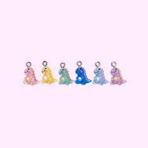 May include: A set of six small, translucent dinosaur charms in pink, yellow, teal, dark blue, light blue, and purple. Each dinosaur figure features a smiling face, a yellow belly patch, a row of spikes along its back, and a silver metal jump ring.