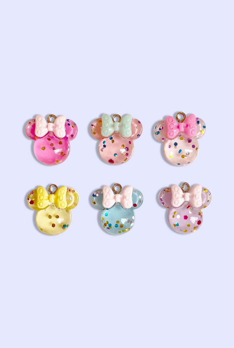 May include: Six mouse-shaped charms made of translucent resin with embedded colorful glitter. Each charm features a solid-colored bow on top and a small gold-toned metal loop for attachment. The colors include pink, light green, clear, yellow, blue, and purple.