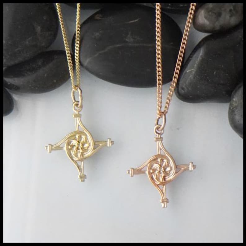 May include: Two Celtic knot pendants on chains, one gold and one rose gold. The pendants are in the shape of a cross with a spiral design in the center.