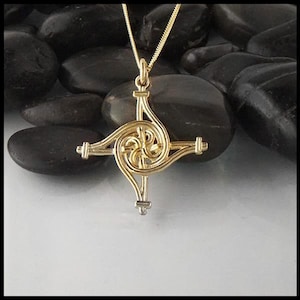 May include: A gold Celtic knot cross pendant with a spiral design. The pendant is on a chain and is resting on black stones.