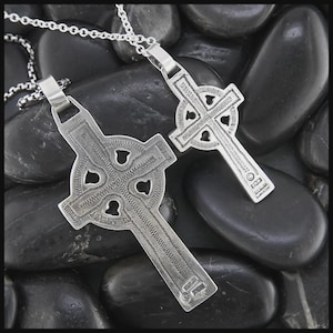 May include: Two silver Celtic cross pendants on chains. The crosses have detailed knotwork designs and are set against smooth, dark stones. The pendants feature cut-out shapes and textured surfaces, reflecting traditional Celtic artistry.