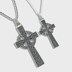 May include: Two silver Celtic cross pendants featuring detailed knotwork patterns. Each cross hangs from a chain, one with a black and silver chain and the other with a silver chain. The crosses have a circular element at the centre.