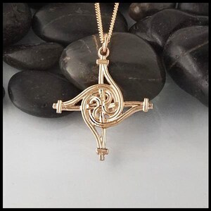 May include: Gold Celtic knot pendant necklace with a spiral design. The pendant is on a chain and is resting on a bed of smooth, gray stones.