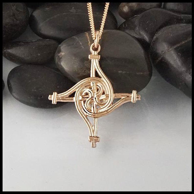 May include: Gold Celtic knot pendant necklace with a spiral design. The pendant is on a chain and is resting on a bed of smooth, gray stones.