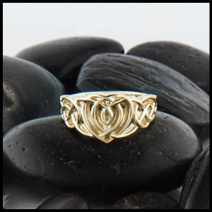Puede incluir: Un anillo de plata con un nudo celta y un diseño de corazón. El anillo está colocado sobre un fondo de piedras negras.