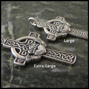 May include: Two silver Celtic cross pendants with a Claddagh design. The larger pendant is labeled "Large" and the smaller pendant is labeled "Extra-Large".