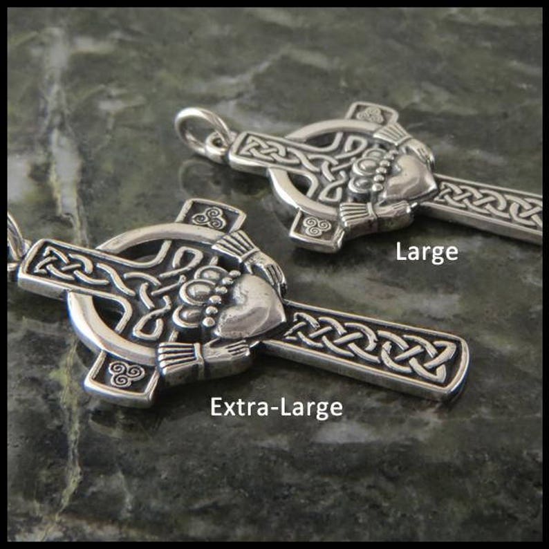 May include: Two silver Celtic cross pendants with a Claddagh design. The larger pendant is labeled "Large" and the smaller pendant is labeled "Extra-Large".
