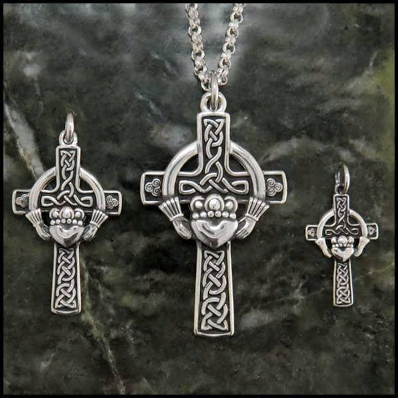 May include: Three silver Celtic cross pendants with intricate knotwork designs. The largest pendant features a Claddagh design with two hands holding a heart. The pendants are on a chain, a table, and a separate surface.