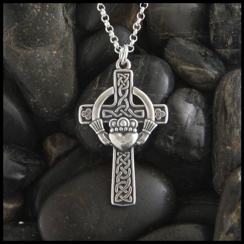 May include: A silver Celtic cross pendant with a knotwork design and a heart-shaped center. The cross is surrounded by a circle with a knotwork design. The pendant is on a silver chain.