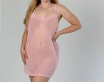 May include: A woman wearing a pink, sheer, sleeveless slip dress. She is standing with her hand on her hip and looking at the camera.