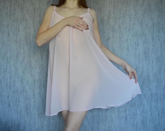 May include: A light pink, sheer nightgown with spaghetti straps. The short, flowing garment has a rounded hemline and is made of a lightweight fabric. The nightgown is a solid color and has a simple, elegant design.