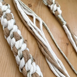 May include: A close-up of a white and brown braided rope with silver accents. The rope is knotted and has a decorative design.