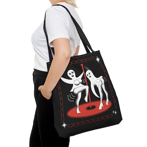 May include: Black tote bag with a white design of two ghosts dancing on a red stage. The ghosts are wearing white outfits and have black eyes. The stage is surrounded by a red chain link fence.