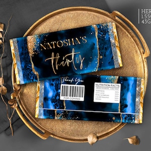 May include: Hershey's 43g chocolate bar with a blue and gold design. The wrapper reads "Natasha's thirty" in gold script. The bar is on a gold tray with a dark grey background. The bar has a barcode and "Thank You" text.