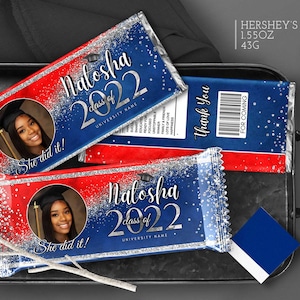 May include: A blue and red chocolate bar wrapper with silver glitter. The wrapper features a photo of a graduate, the text "Nalosha class of 2022", and the words "She did it!"