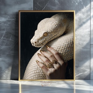 Può includere: Stampa artistica incorniciata raffigurante un serpente bianco con occhi gialli. Una mano con unghie e anelli dorati tocca delicatamente il serpente. L'opera d'arte ha uno sfondo scuro e una cornice dorata. Il testo "Celestiq ART" è in basso a destra.